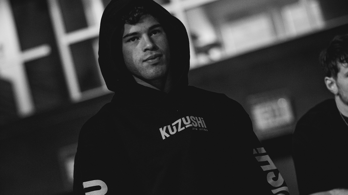 A black Kuzushi branded hoodie worn by a man in a dark, moody indoor setting.